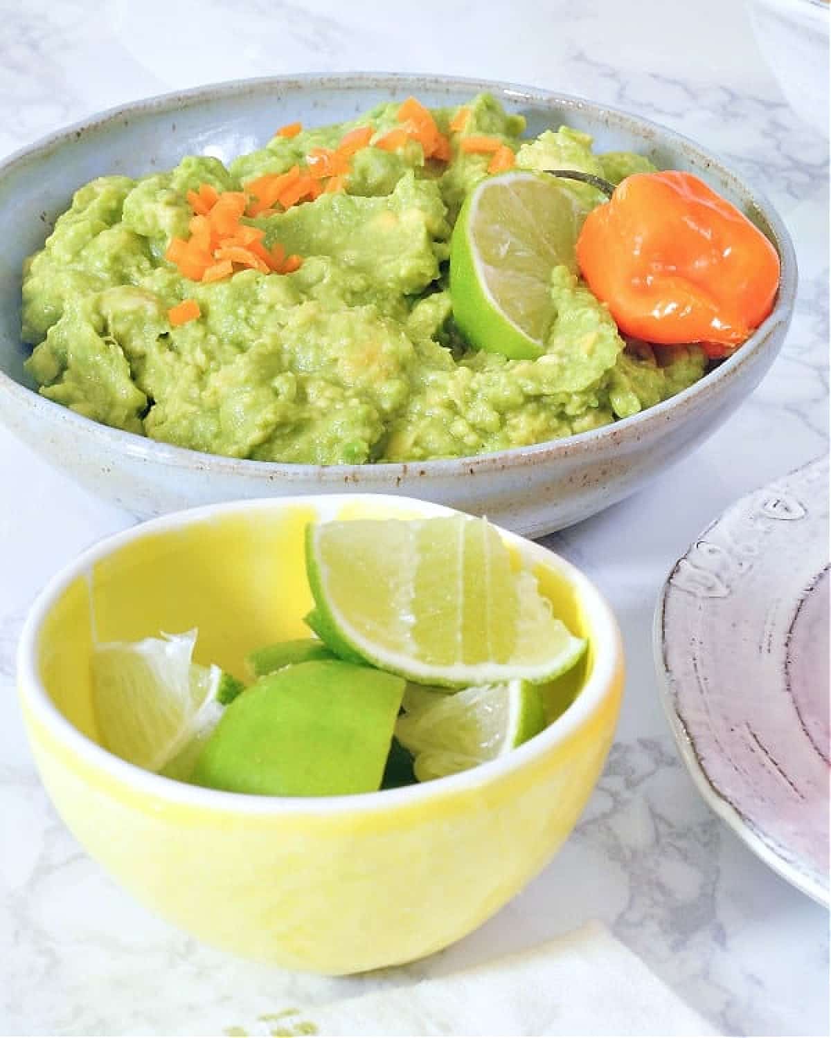 Mango habanero guacamole served in a shallow grey bowl. A smaller bowl of lime wedges on the side.