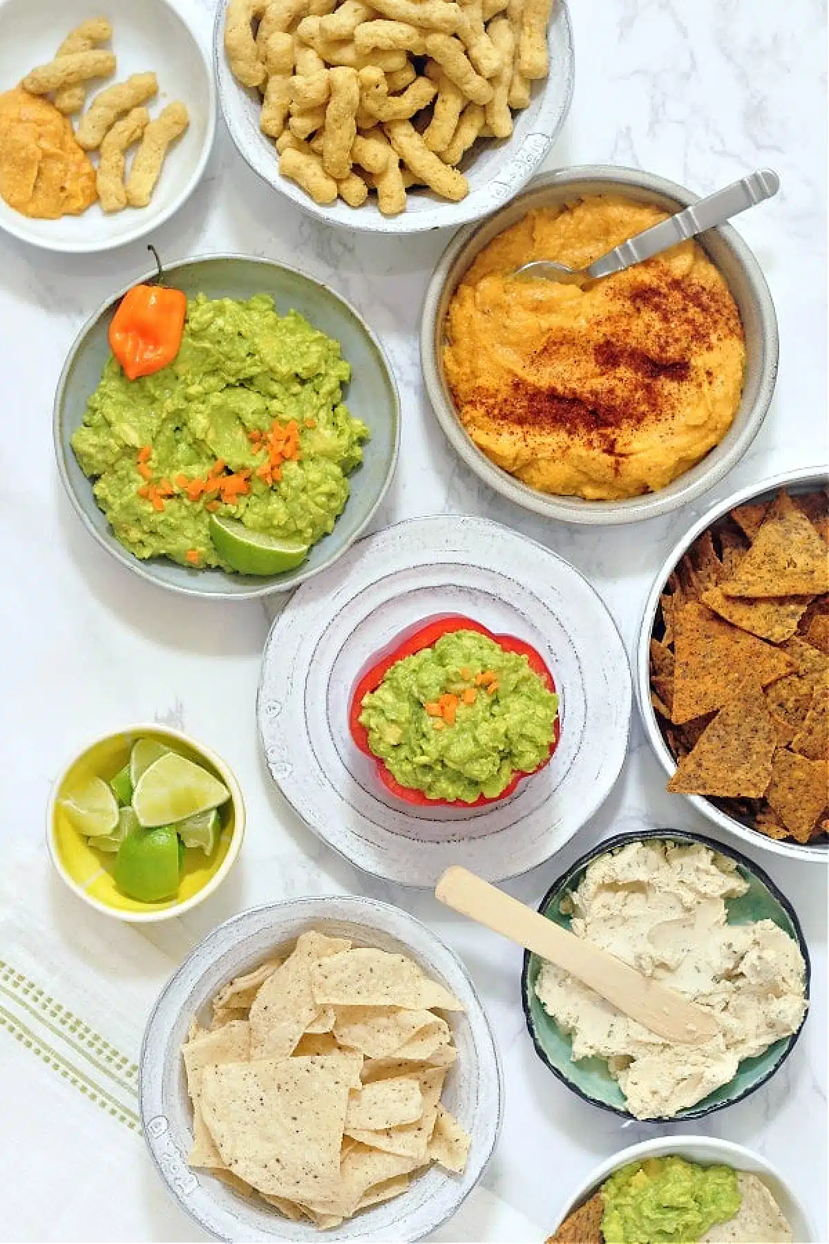 Overhead view of mango habanero guacamole served in a hollowed out red bell pepper. Smaller bowls of lime wedges, other dips, chips and crackers on the side.