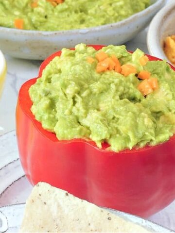 Mango habanero guacamole served in a hollowed out red bell pepper. A smaller bowl of lime wedges on the side.