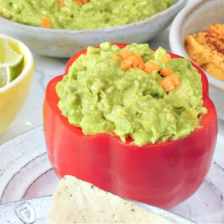 Mango habanero guacamole served in a hollowed out red bell pepper. A smaller bowl of lime wedges on the side.