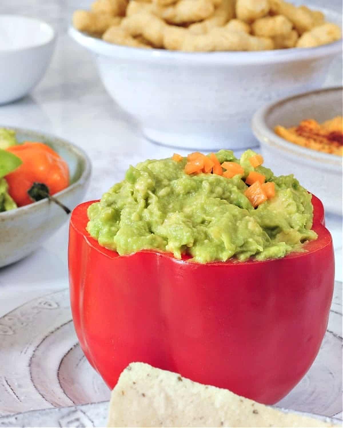 Mango habanero guacamole served in a hollowed out red bell pepper. A smaller bowl of crackers on the side.