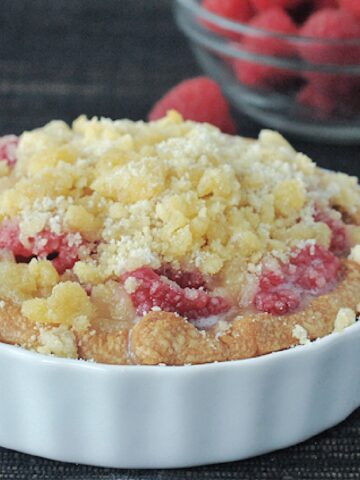Raspberry cream crumble pie in a small white ramekin, with a small glass bowl of fresh raspberries in background.