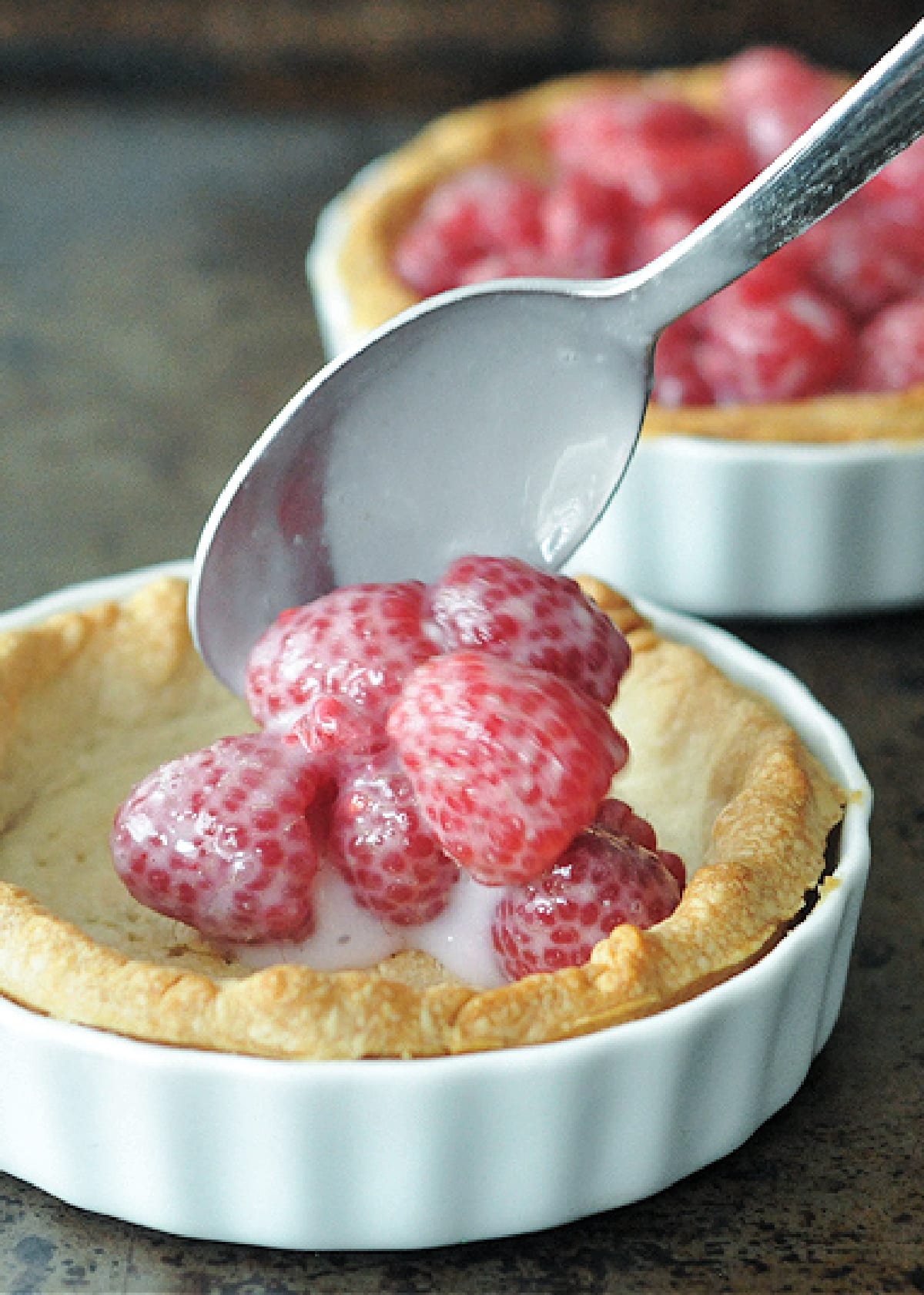 How to make raspberry crumble pie: a spoon adding raspberries and cream to a par-baked pie crust.