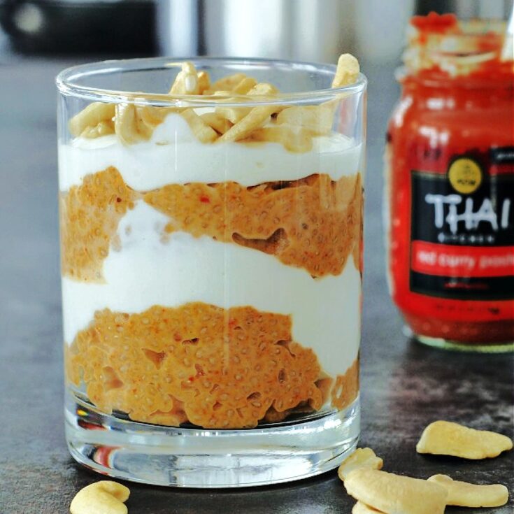 Red curry coconut chia pudding and cashew cream layered in a glass, red curry paste jar in background.