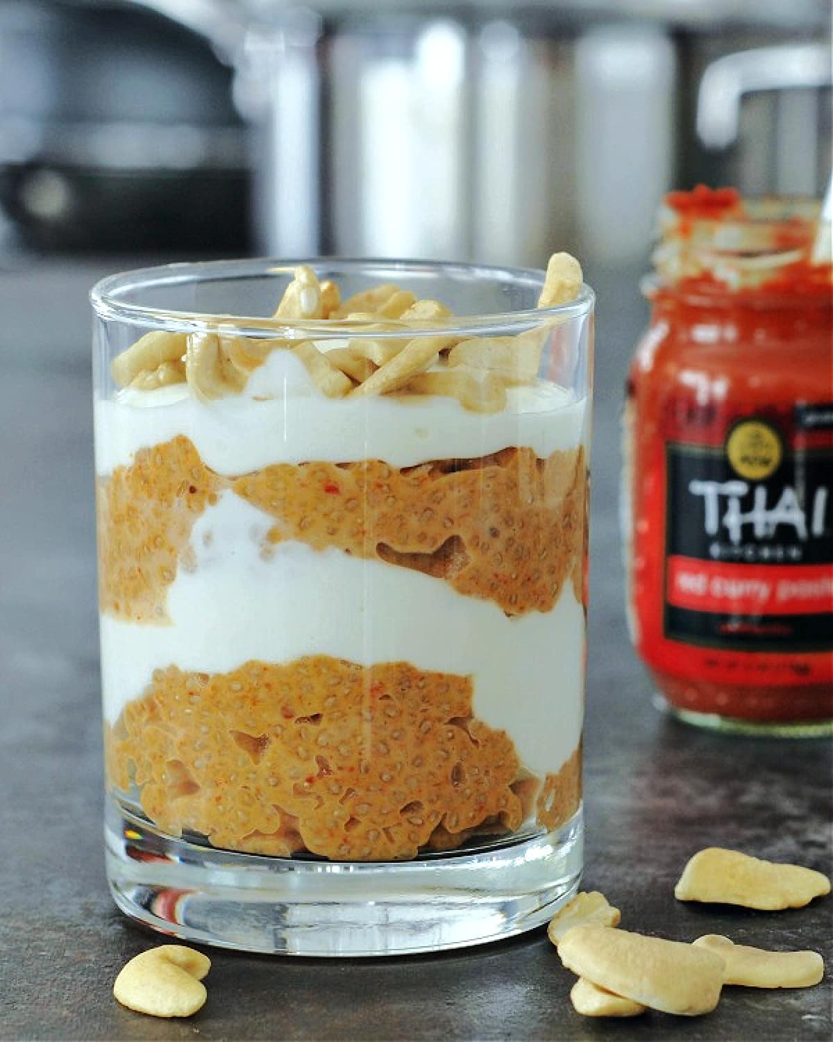 Red curry coconut chia pudding and cashew cream layered in a glass, red curry paste jar in background.