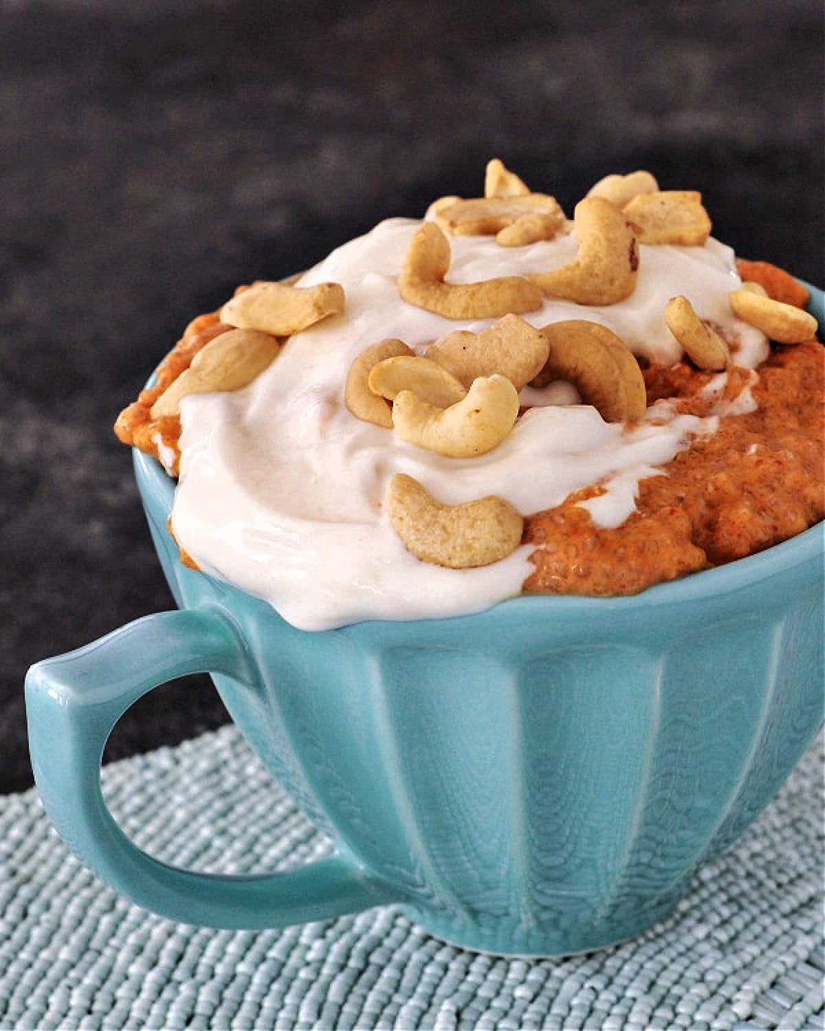 Savory red curry chia pudding and cashew cream, topped with cashews, served in a teal mug.