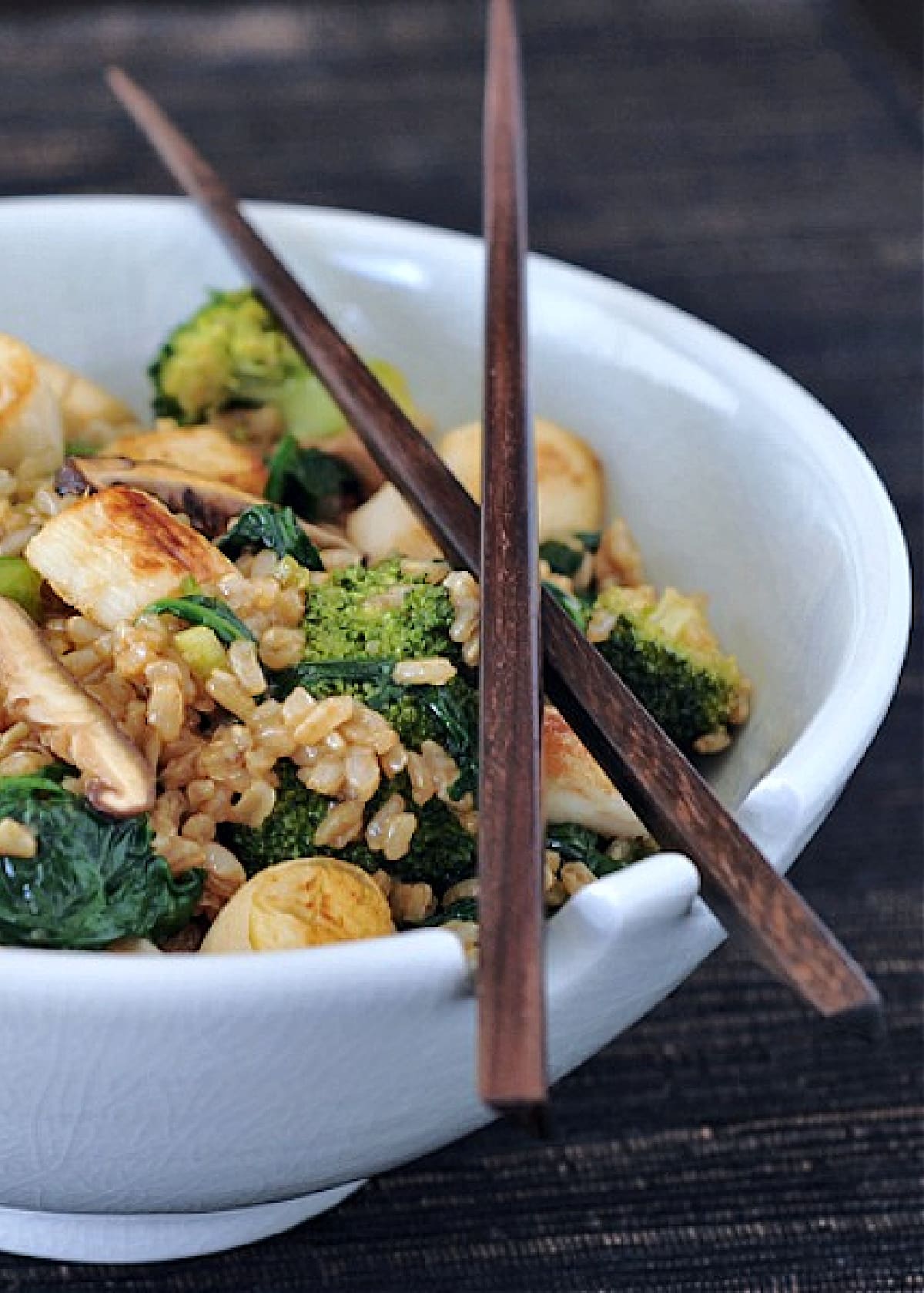 Vegan scallop fried rice in a bowl with chopsticks: vegan "scallops" made from hearts of palm, sliced shiitake mushroom, broccoli trees, sliced green onion, golden fried rice.