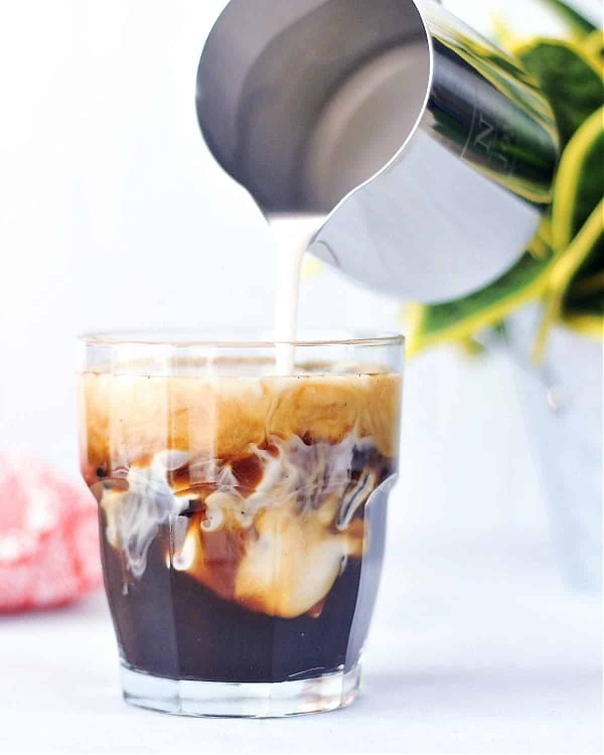 Coconut cold brew over ice in a short rocks glass, coconut milk being poured in.