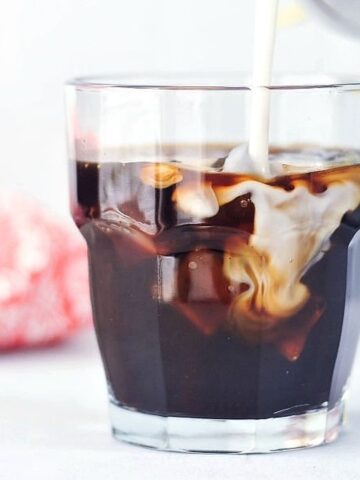 Simple coconut cold brew over ice in a short rocks glass, coconut milk being poured in.