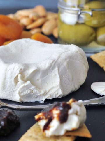 Soy free vegan cream cheese on a cheese board with olives, apricots, jam and crackers.