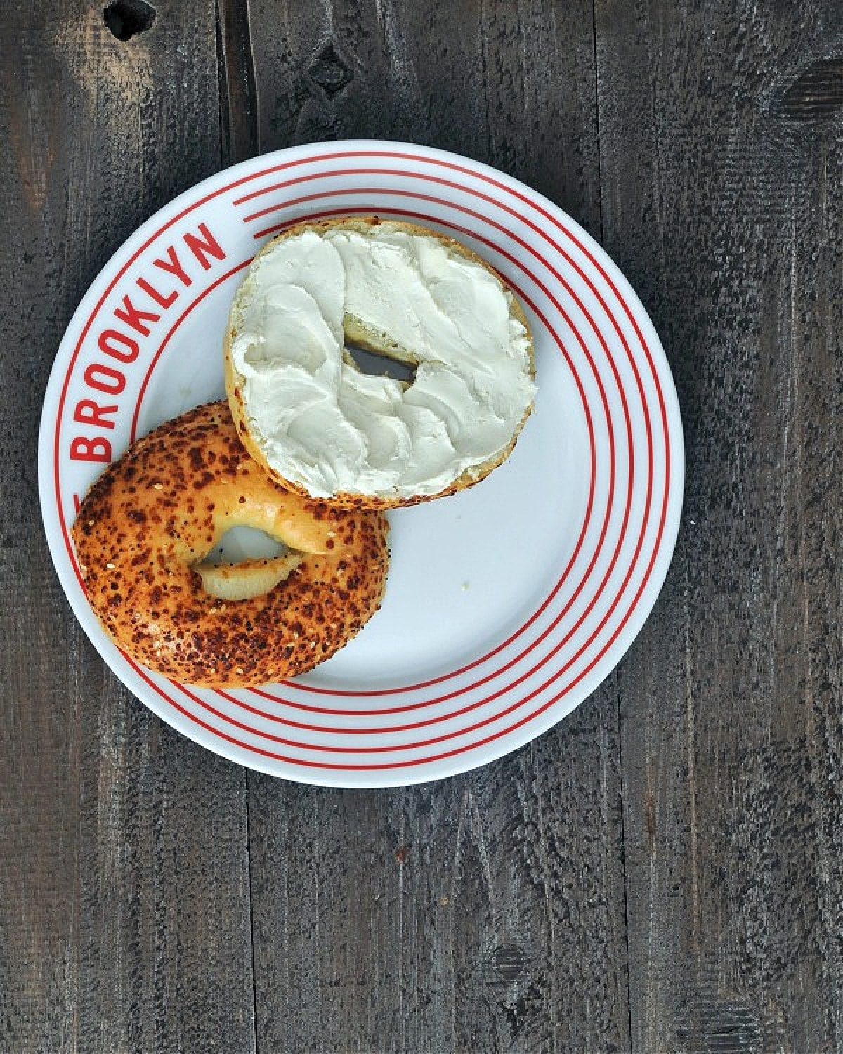Dairy free cream cheese spread on a bagel, on a white plate that says BROOKLYN in red.