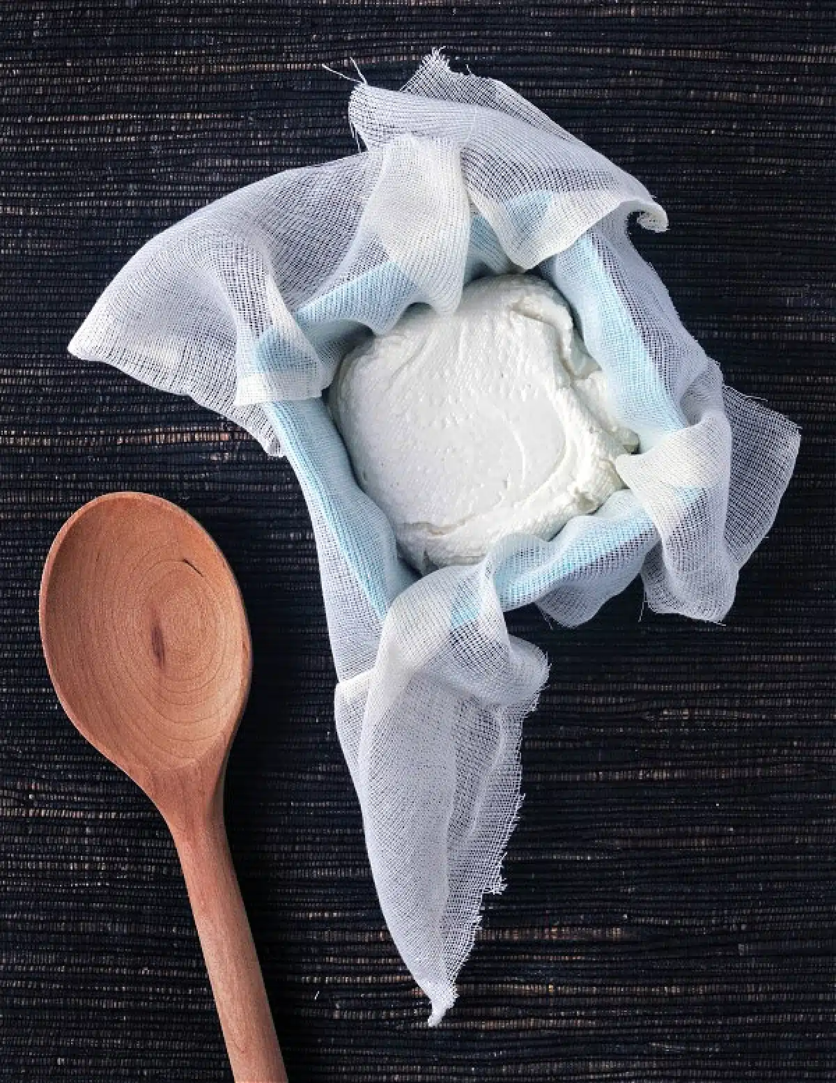 Overhead view of making vegan cream cheese: the mixture wrapped in cheesecloth and placed inside a ceramic container to ferment.