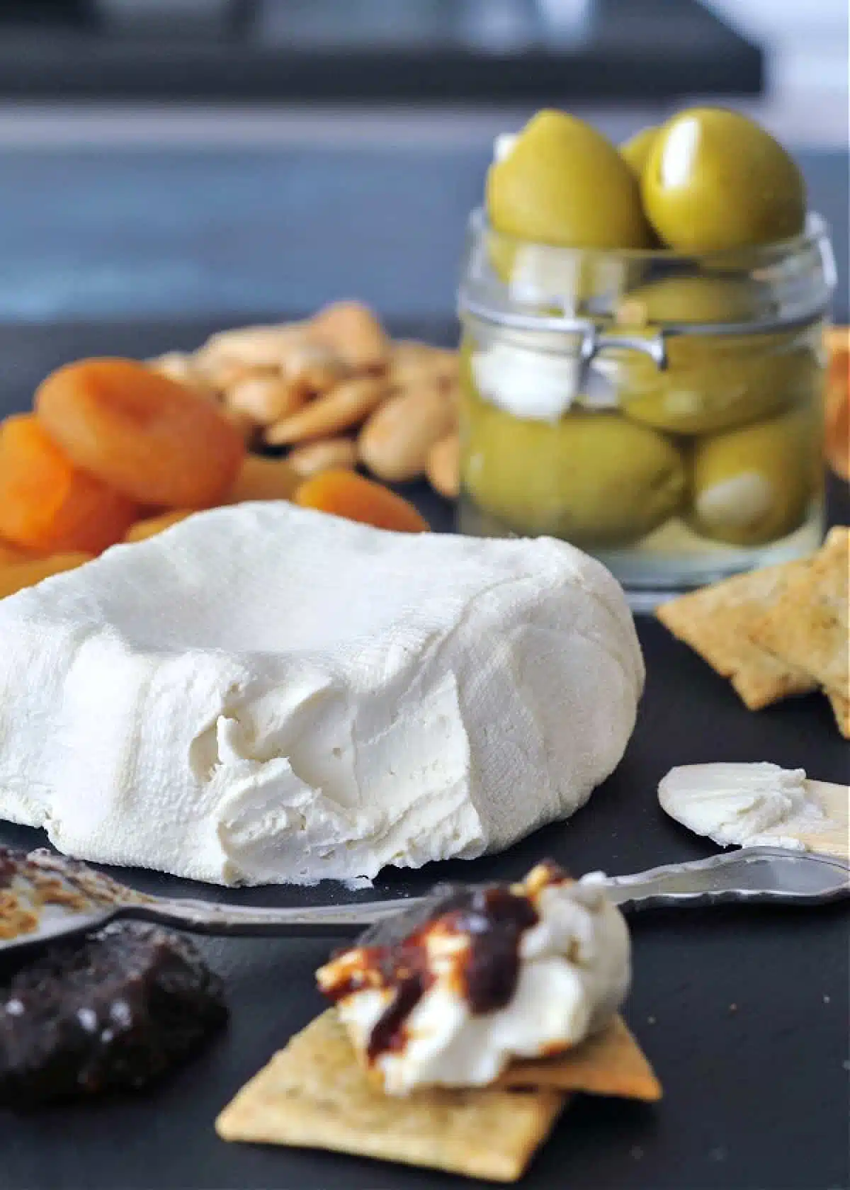 Soy free vegan cream cheese on a cheese board with olives, apricots, jam and crackers.