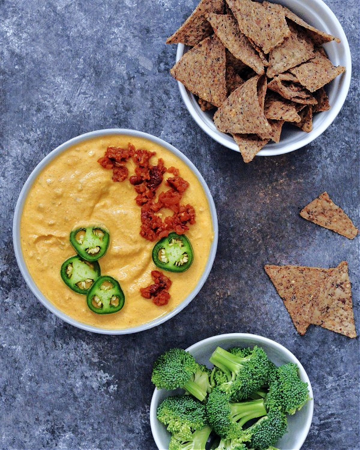 Overhead view of spicy vegan chorizo queso in a bowl with chips and broccoli for dipping.