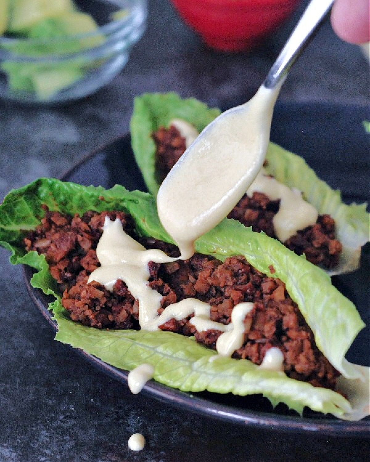 Vegan chorizo sausage in lettuce wraps with avocado slices and dairy free cheese sauce being spooned on top.