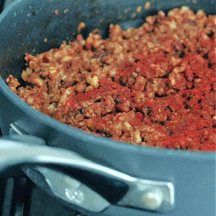 Vegan chorizo sausage in a skillet over a gas cooktop flame.