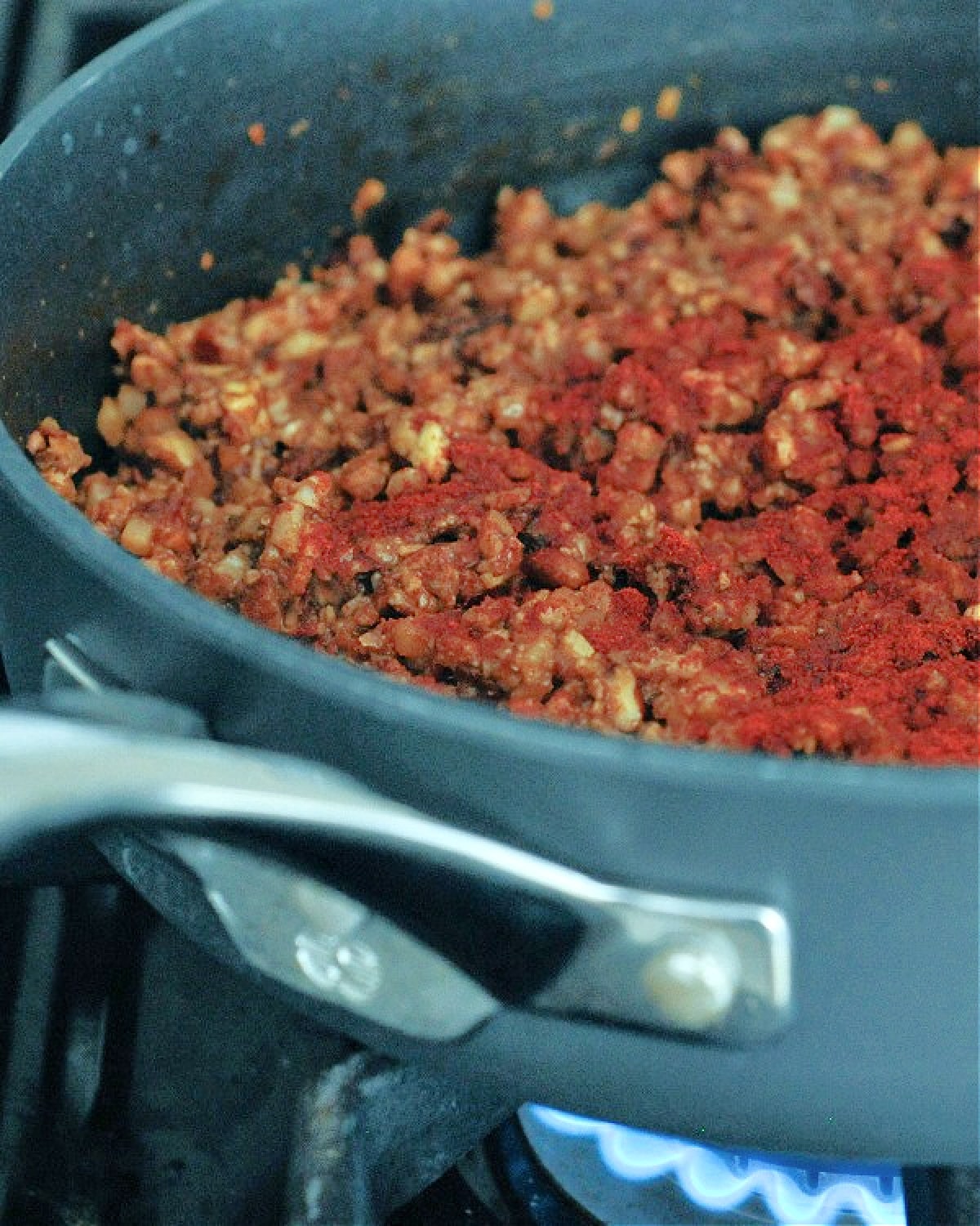 Vegan chorizo sausage in a skillet over a gas cooktop flame.