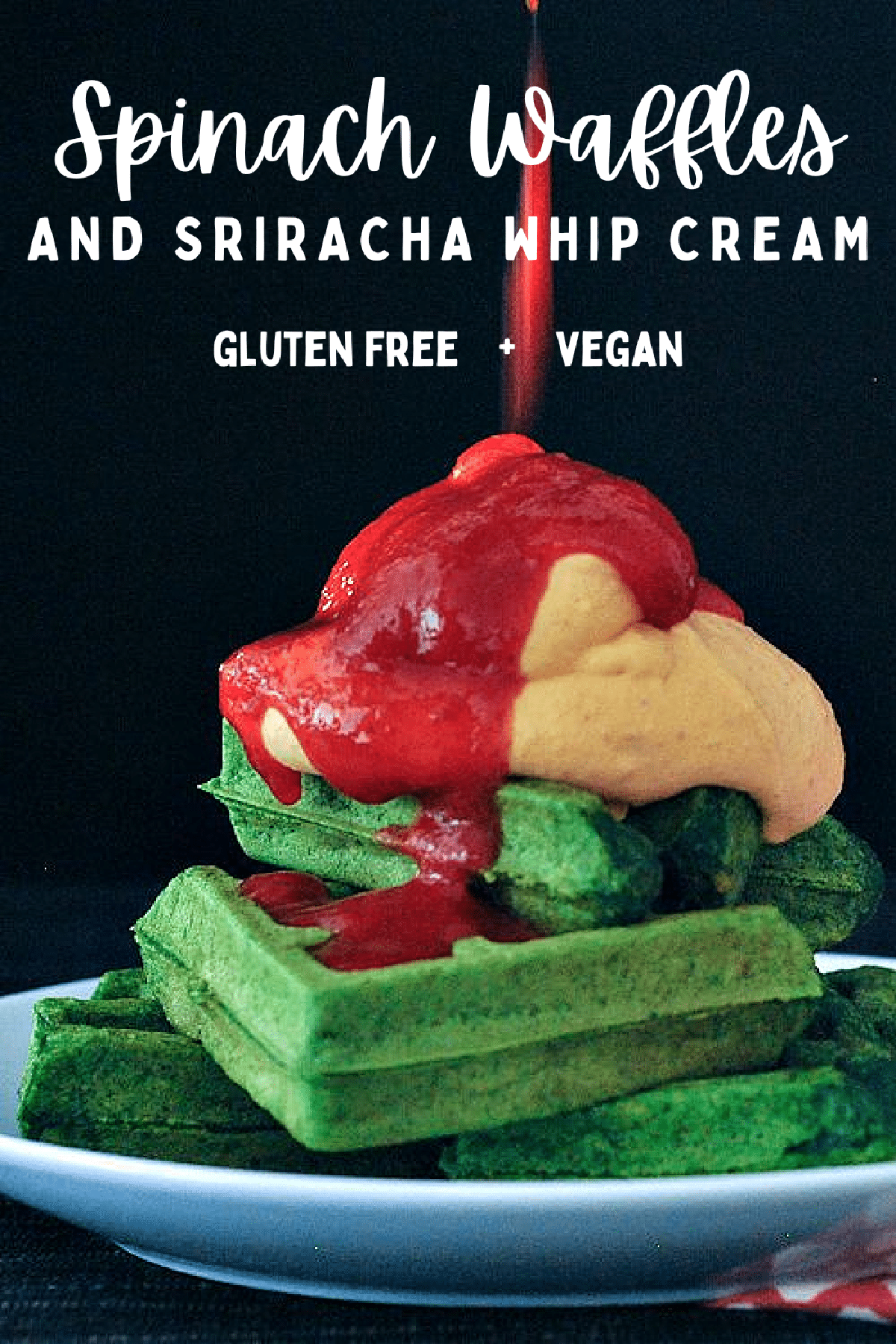 Bright green spinach waffles stacked three high on a white plate, topped with orange colored sriracha whip cream and bright red sriracha sauce.