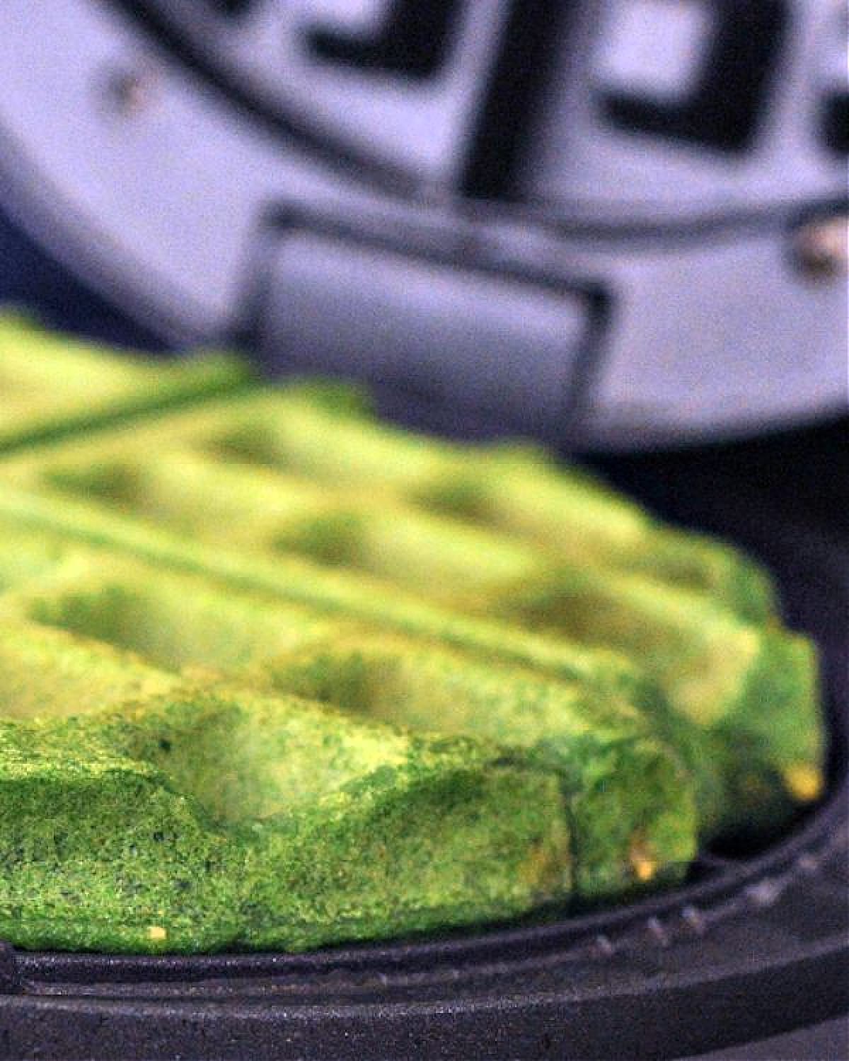 Bright green spinach waffle in an open waffle maker.