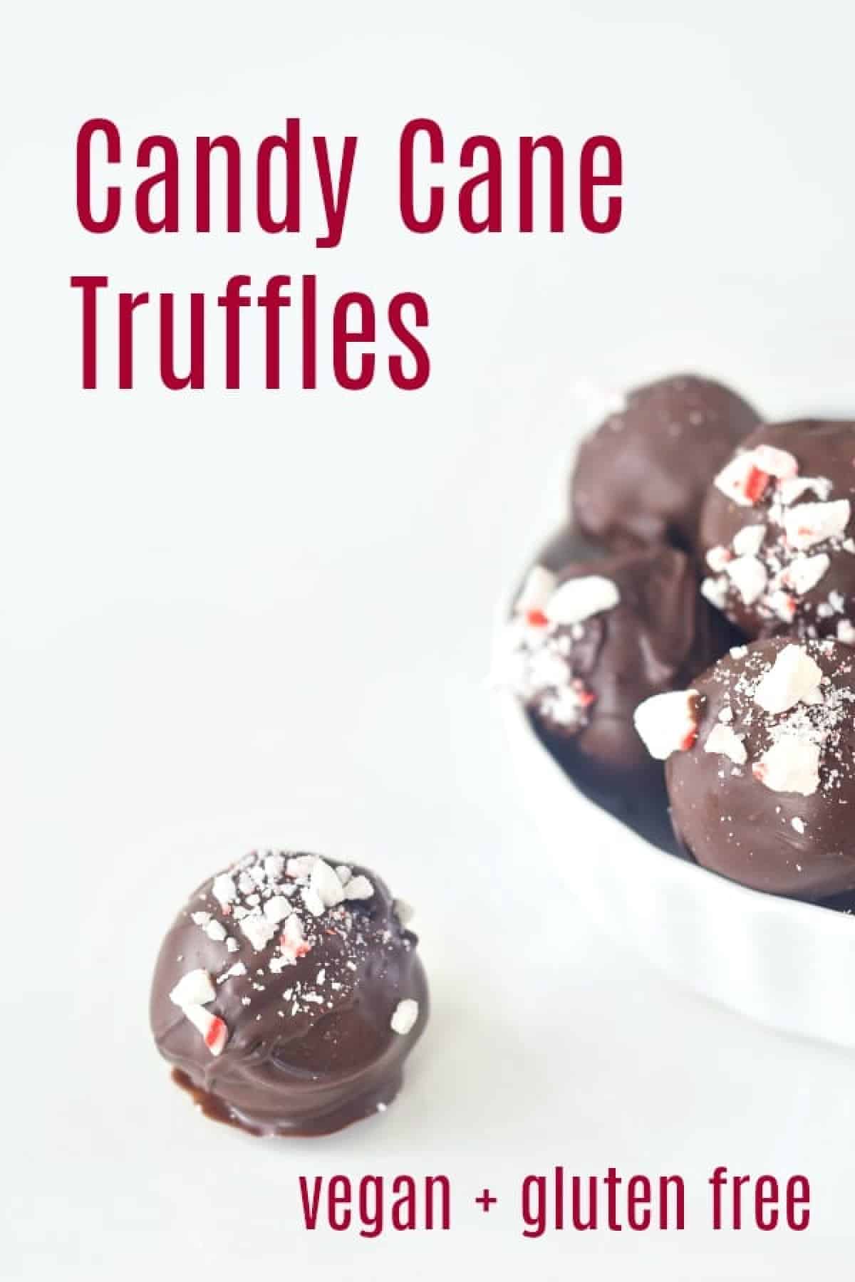 A small ramekin of chocolate coated truffles with candy cane pieces on top sits on a white tabletop. One single truffle sits outside the bowl.
