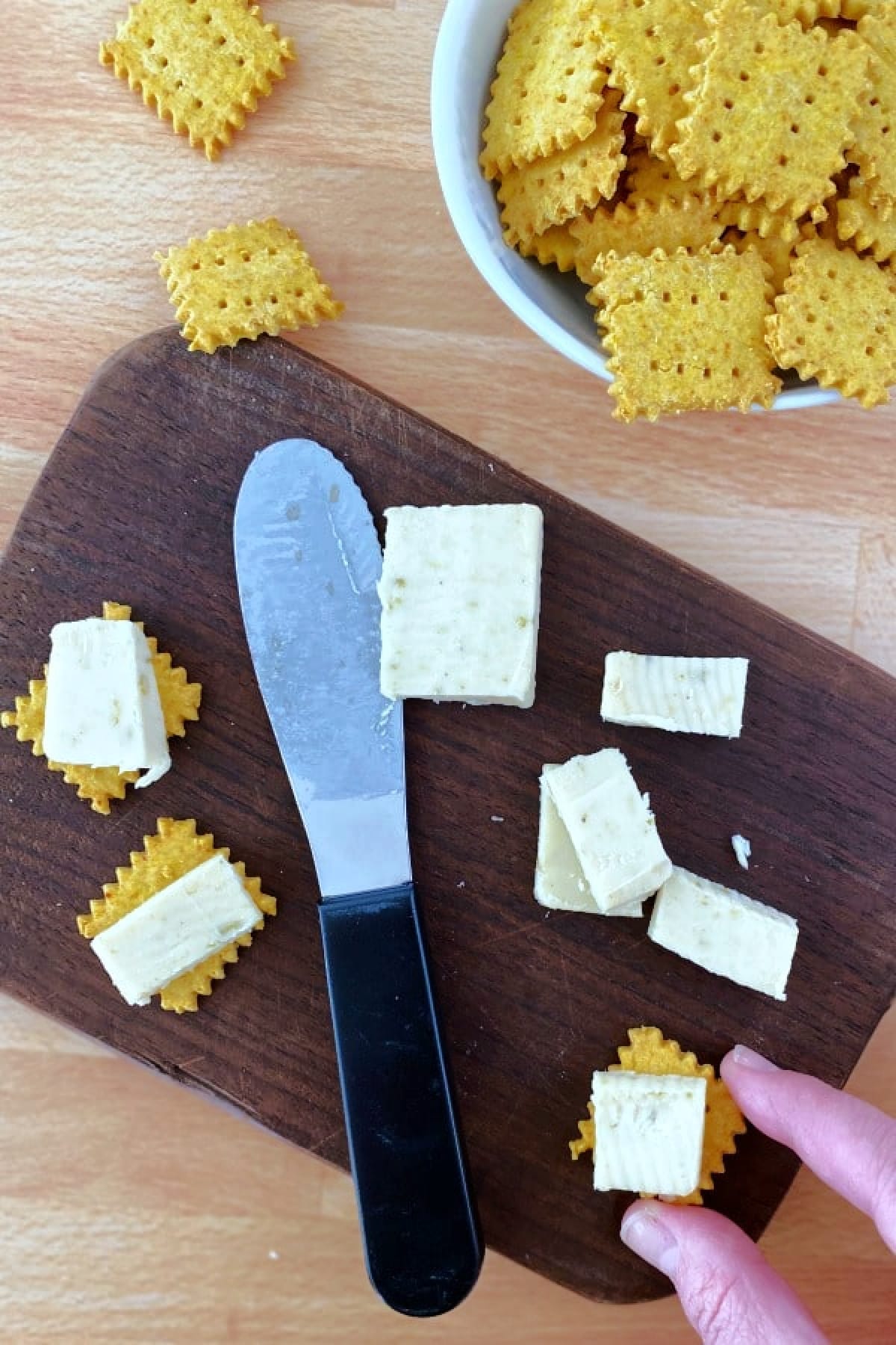 A board with vegan cheese crackers, cheese, and a knife.