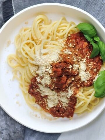 Overhead view of vegan meat crumbles in red sauce on spaghetti noodles, garnished with fresh basil leaves.