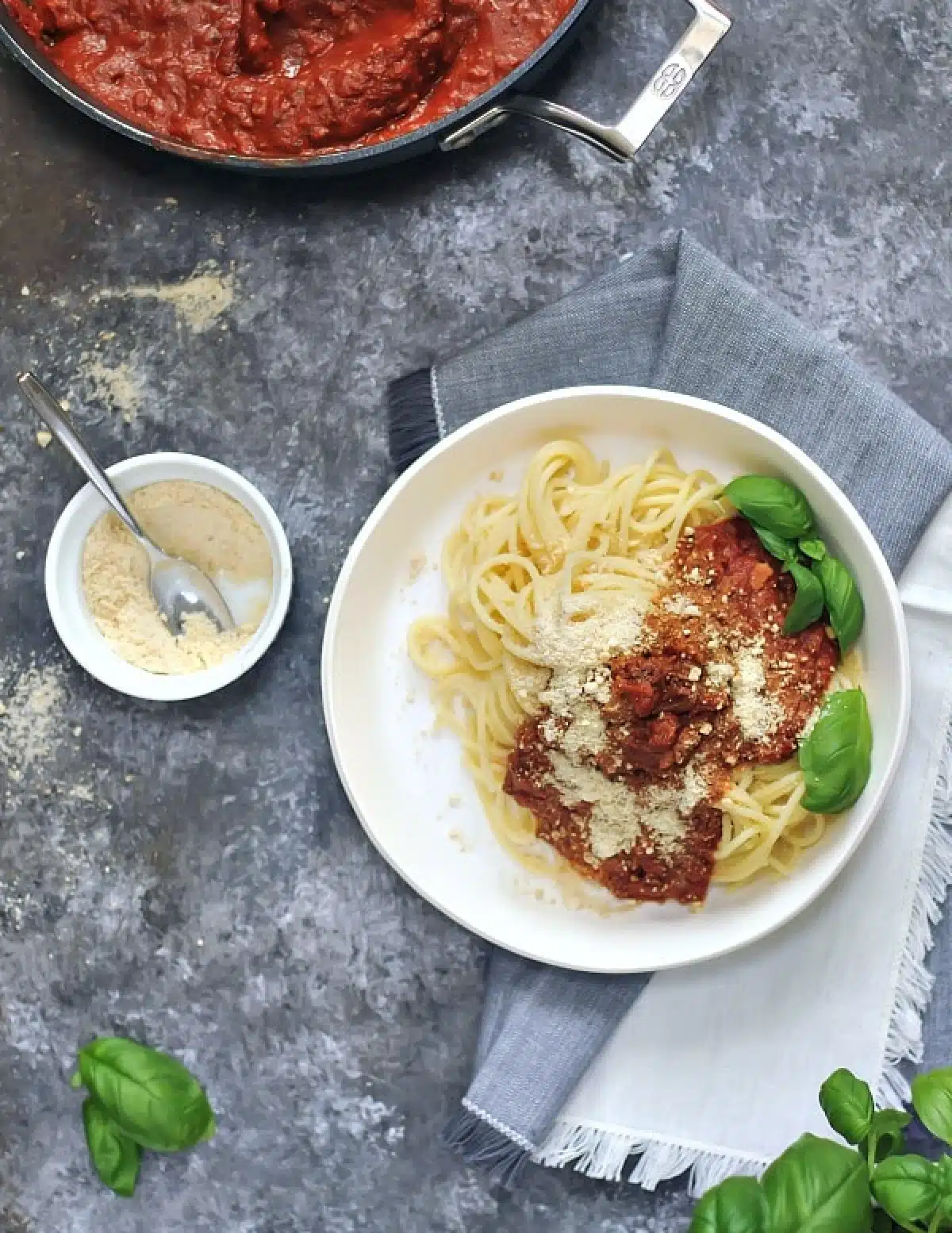 Overhead view of vegan meat crumbles in red sauce on spaghetti noodles, garnished with fresh basil leaves.