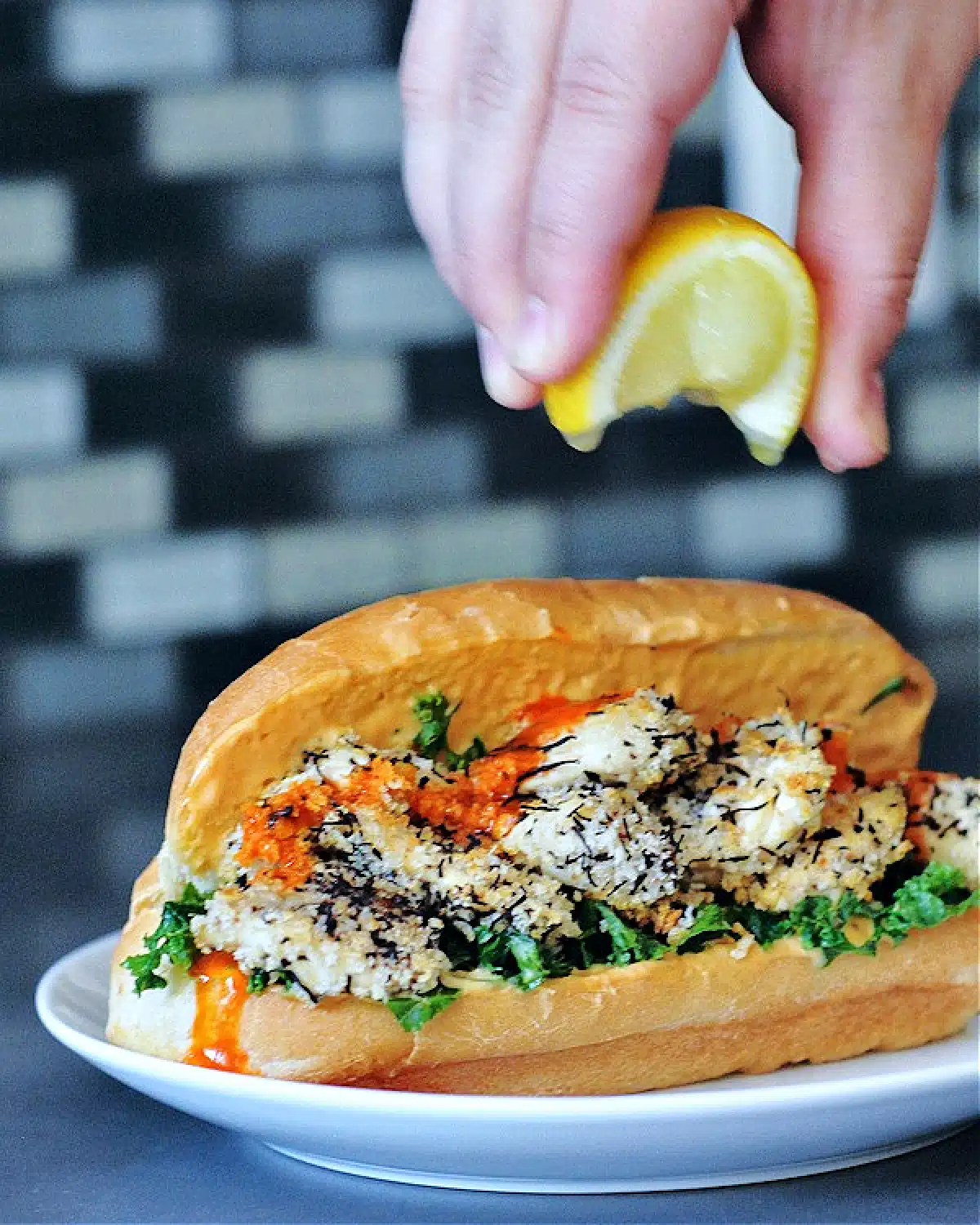 A hand squeezing lemon over a vegan oyster mushroom po boy sandwich, dressed with kale and spicy garlic sauce.