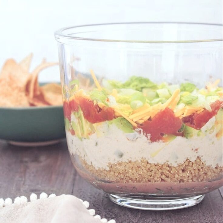 Side view of all the layers in seven layer dip: beans, quinoa, cashew cheese sauce, avocado, tomato, green onions and lettuce.