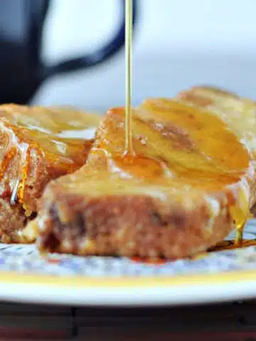 French toast on an colorful Italian plate, with syrup being poured on top. A navy blue coffee mug sits blurred in background.