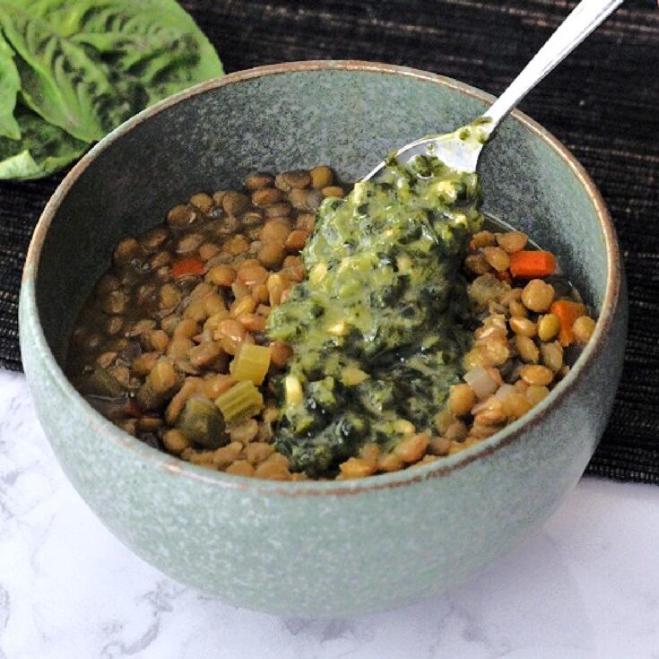 Close up of a dark grey bowl with vegetable lentil soup topped with a chunky basil sauce.