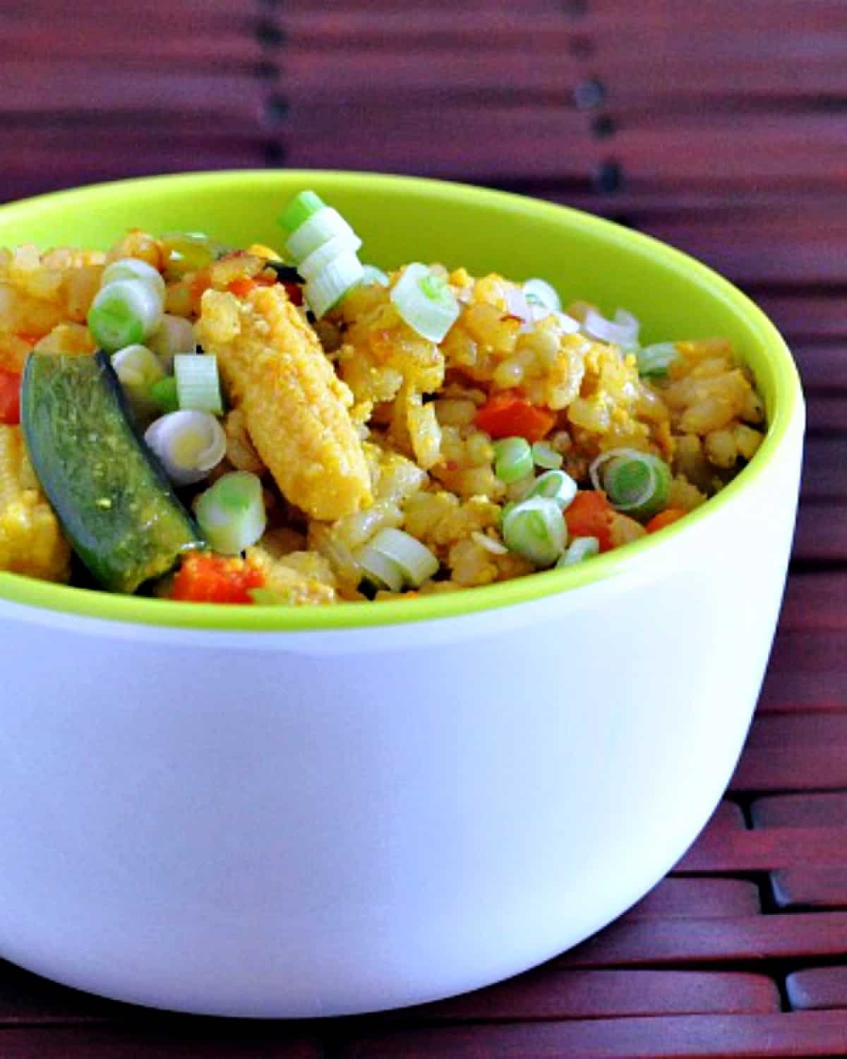 Veggie fried rice in a white bowl with bright green rim: pea shoots, baby corn, diced carrot, golden fried rice.