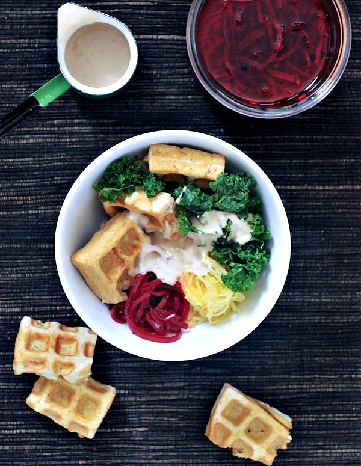 Overhead view of a veggie bowl with waffled tofu (spaghetti squash, roasted beet ribbons, marinated kale, and tofu cooked in the waffle maker) with a tahini sauce drizzled over top.