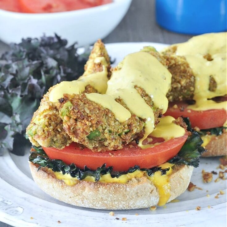 Avocado kale florentine is fried avocado slices with tomato and kale on an English muffin half, hollandaise sauce on top.