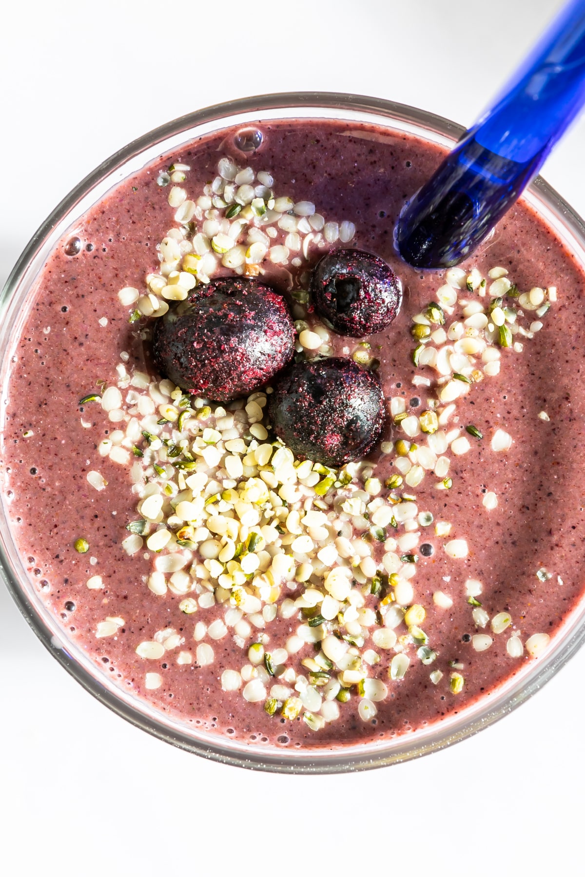 Overhead view of purple blueberry smoothie in pint glass topped with frozen blueberries and hemp seeds.
