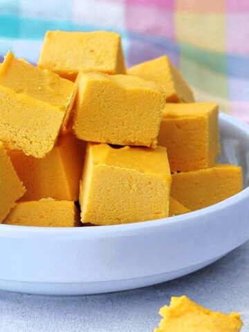 A small light blue shallow bowl filled with squares of butternut toffee fudge, a pastel plaid napkin in the background.