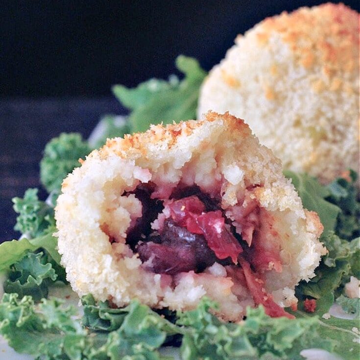 Close up inside view of crispy stuffed potato balls - sitting on curly kale on a white plate, this panko crusted mashed potato ball is cut in half to show the jackfruit filling.