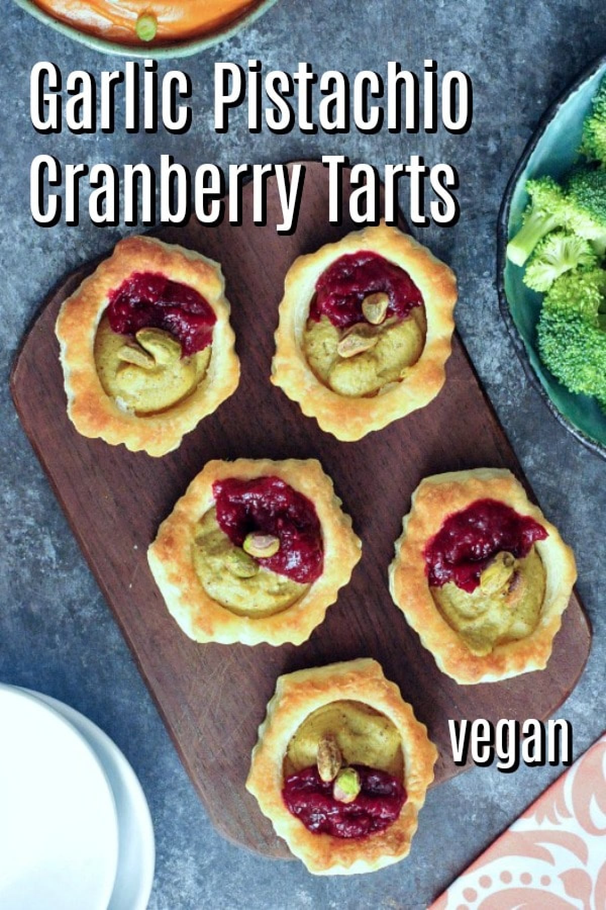 Overhead view of bright pink and green garlic pistachio cranberry tarts on a wood serving board.