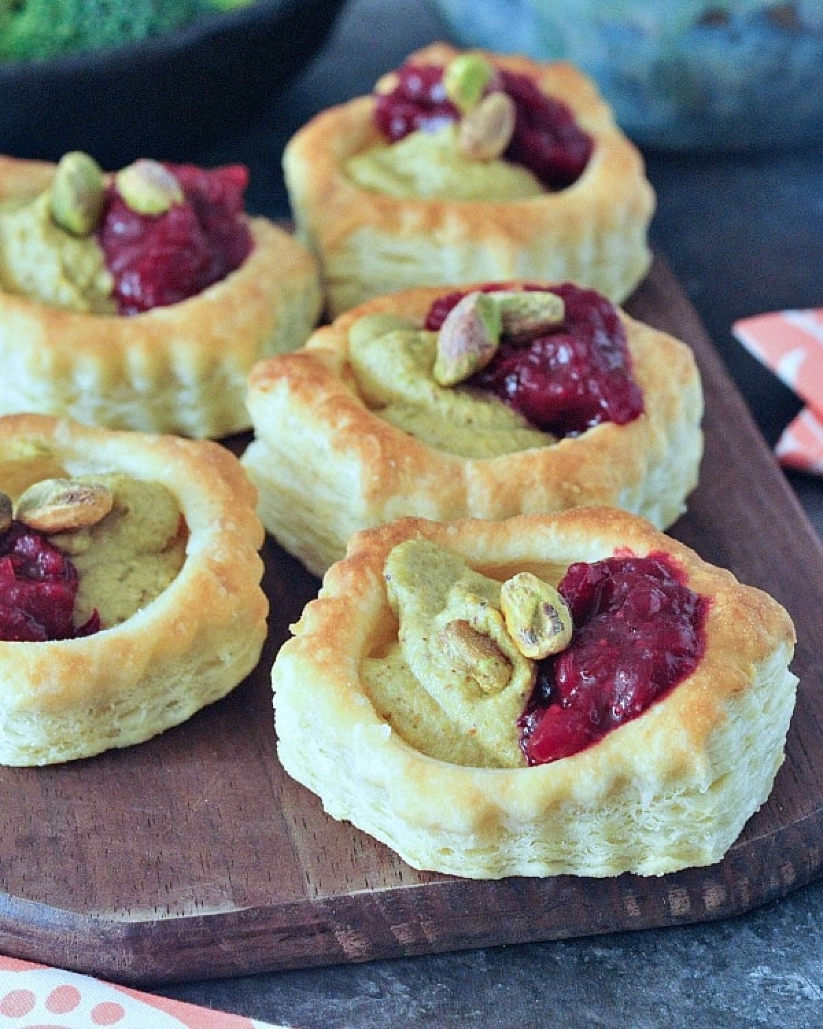 Bright pink and green garlic pistachio cranberry tarts on a wood serving board.