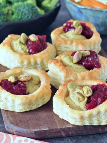 Bright pink and green garlic pistachio cranberry tarts on a wood serving board.