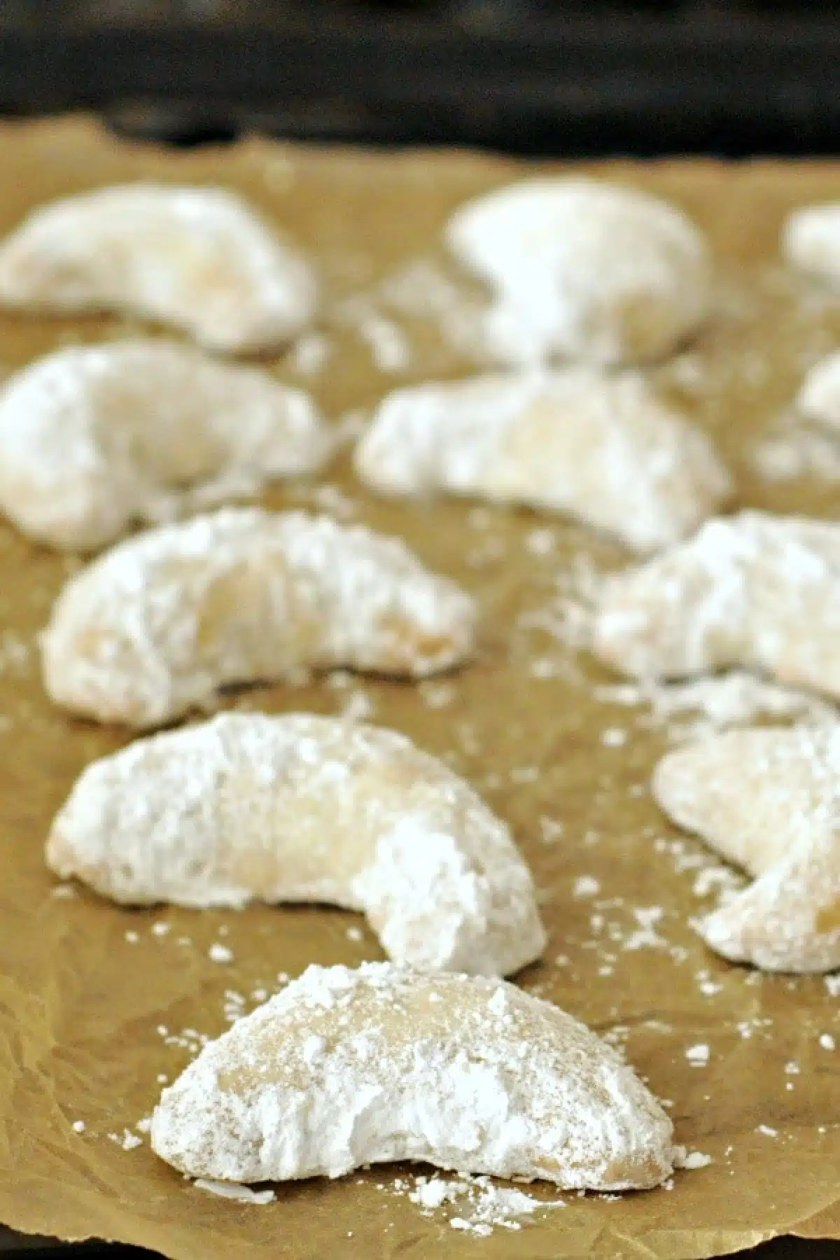 Powdered sugar covered crescent shaped cookies on a parchment lined baking sheet.