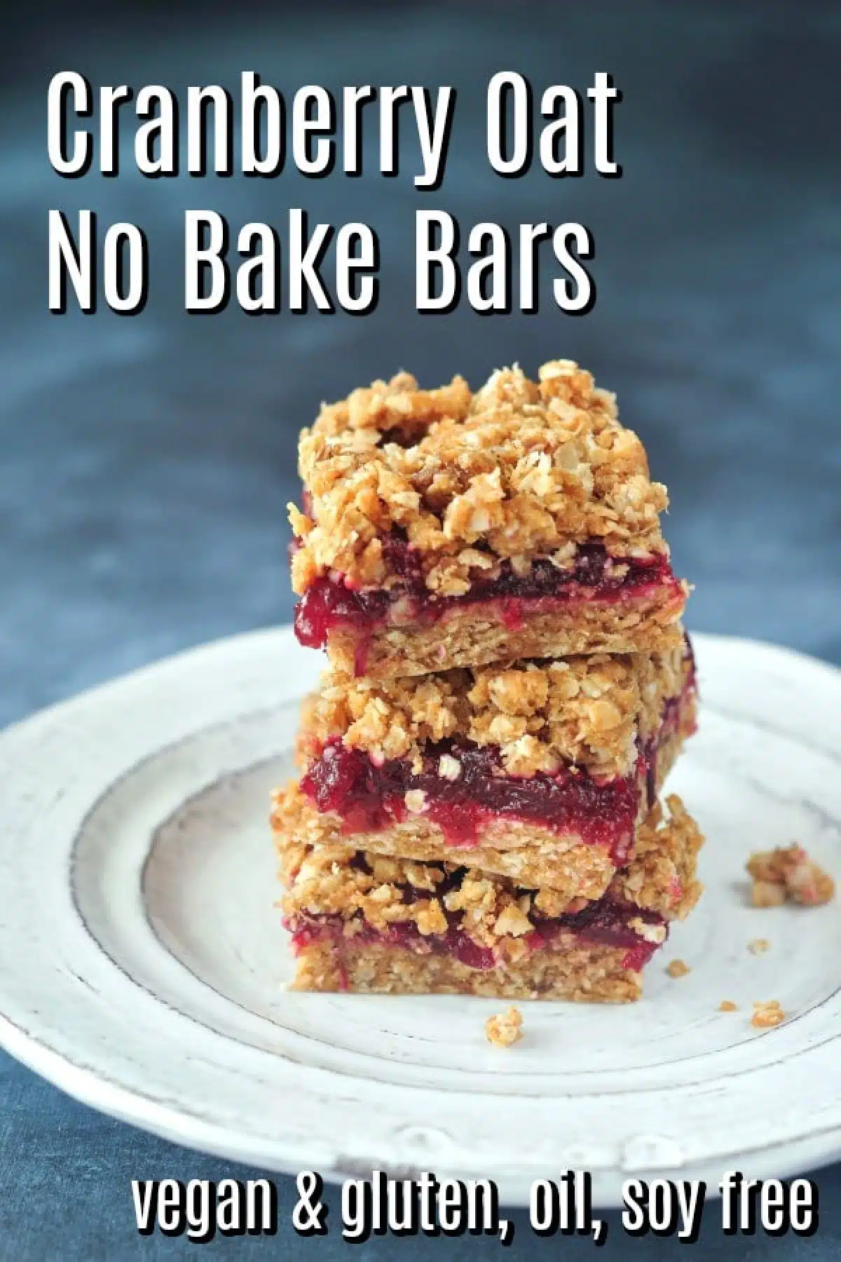 A stack of three cranberry oat no bake bars on a rustic white plate against a dark blue marbled background.