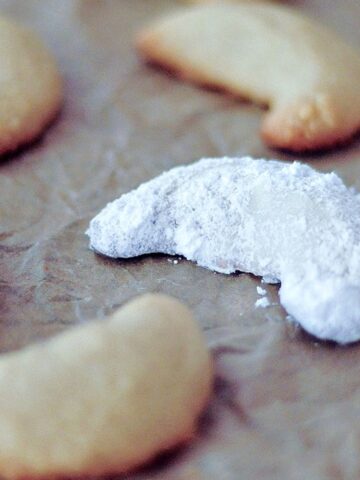 Powdered sugar covered crescent shaped cookies on a parchment lined baking sheet.