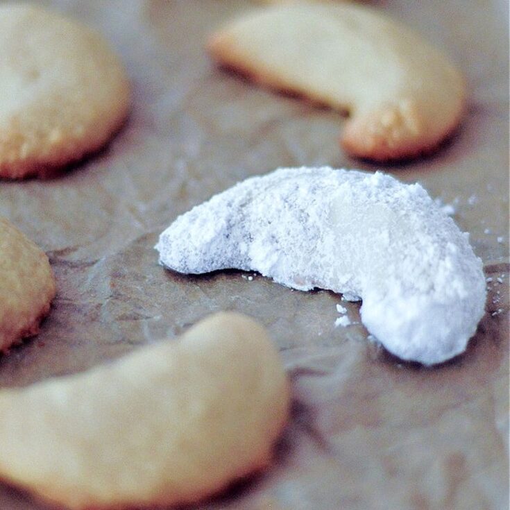 Powdered sugar covered crescent shaped cookies on a parchment lined baking sheet.