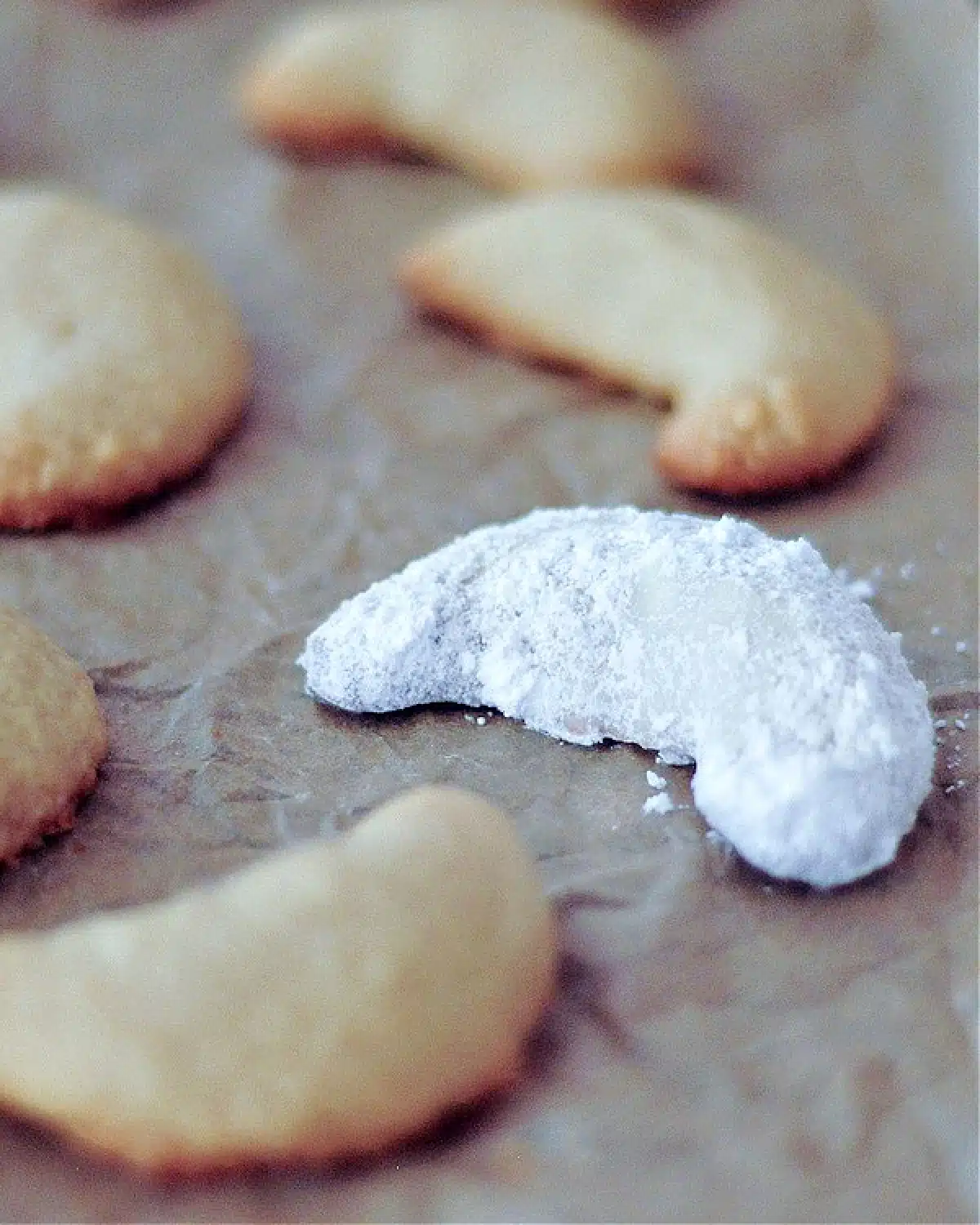 Powdered sugar covered crescent shaped cookies on a parchment lined baking sheet.