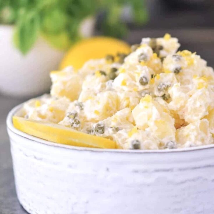 Lemon piccata potato salad in a serving bowl, garnished with a lemon slice, lemon zest, and capers.