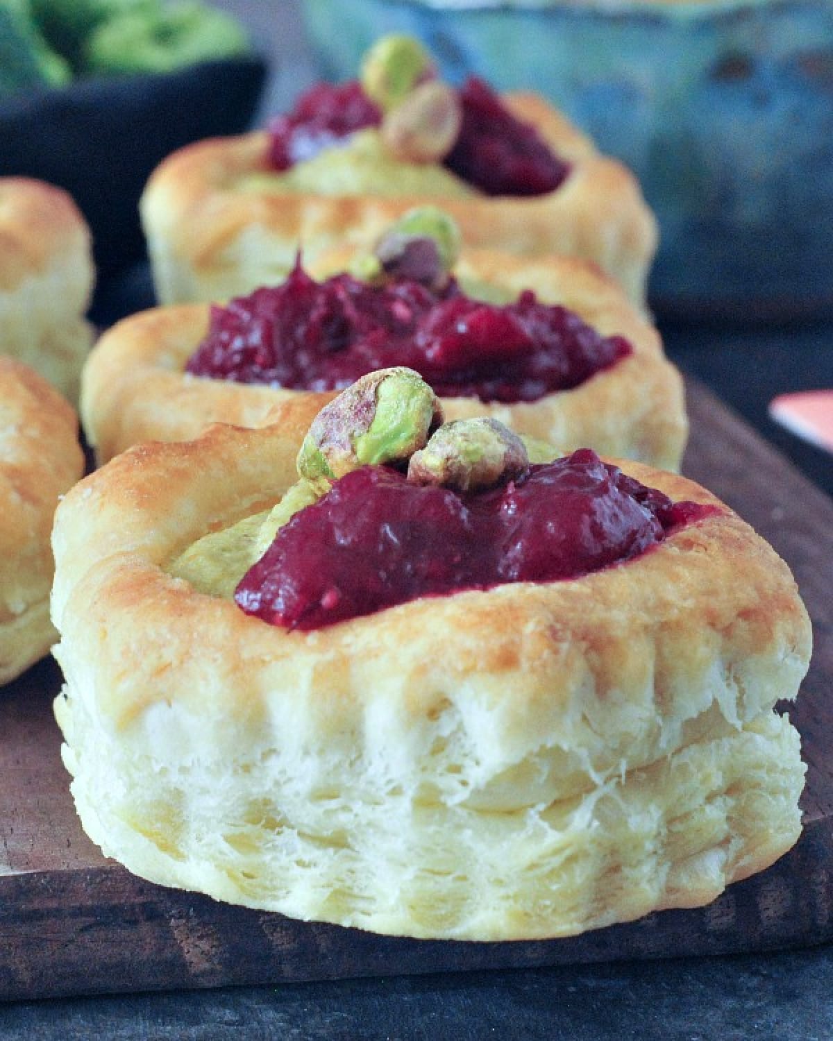 Close up side view of bright pink and green garlic pistachio cranberry tarts on a wood serving board.