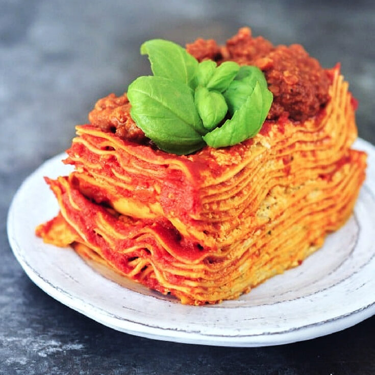 Twelve layer slice of gluten free Vegan Lasagna on a rustic plate, garnished with fresh basil.