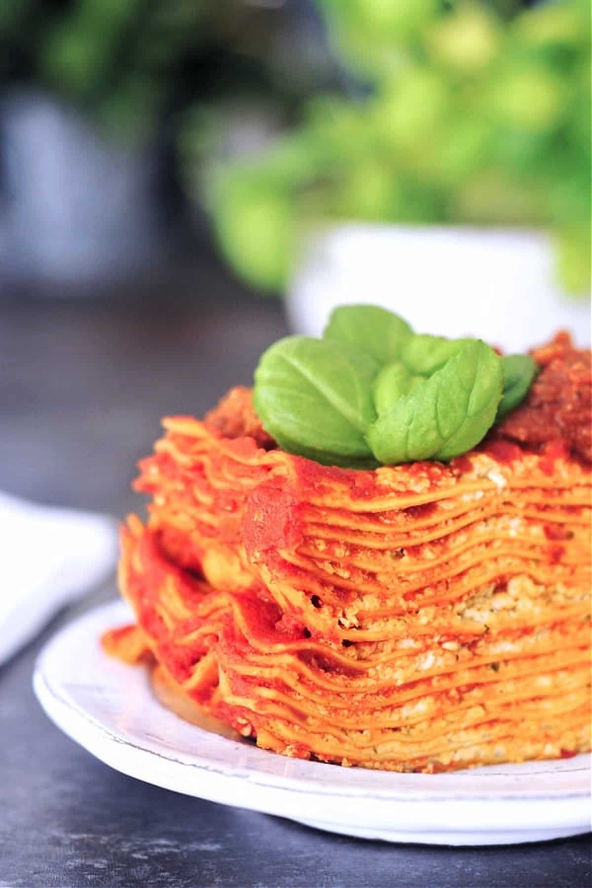 Twelve layer slice of gluten free Vegan Lasagna on a rustic plate, garnished with fresh basil.