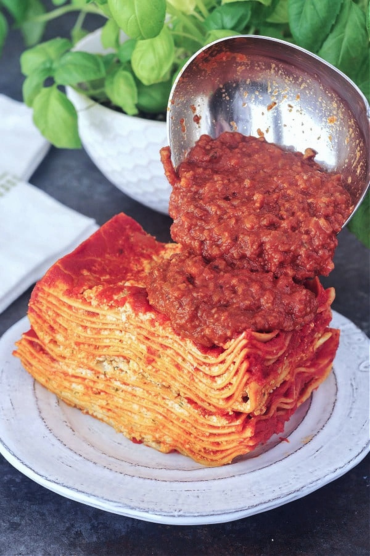 Square of lasagna with meat sauce being poured over top.